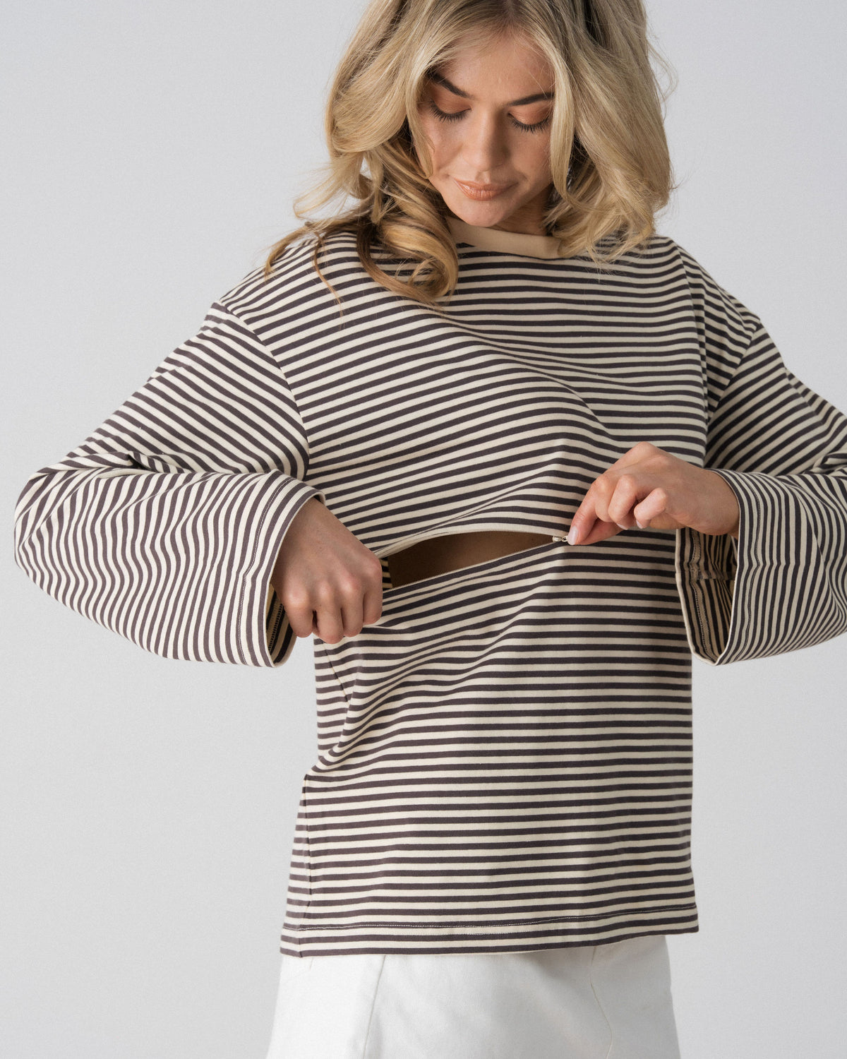 Model opening the hidden two-way underbust zip on the Lenelly Lena striped tee in grey and off-white for discreet breastfeeding access