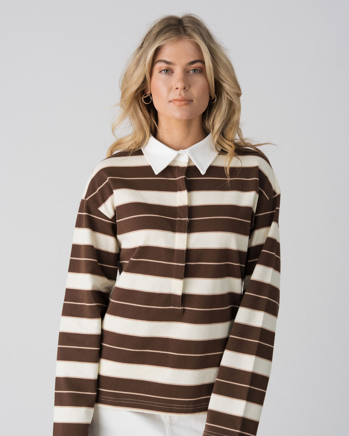 Close-up of the white collar and concealed button placket on the Lenelly Erika rugby polo in brown and cream stripe