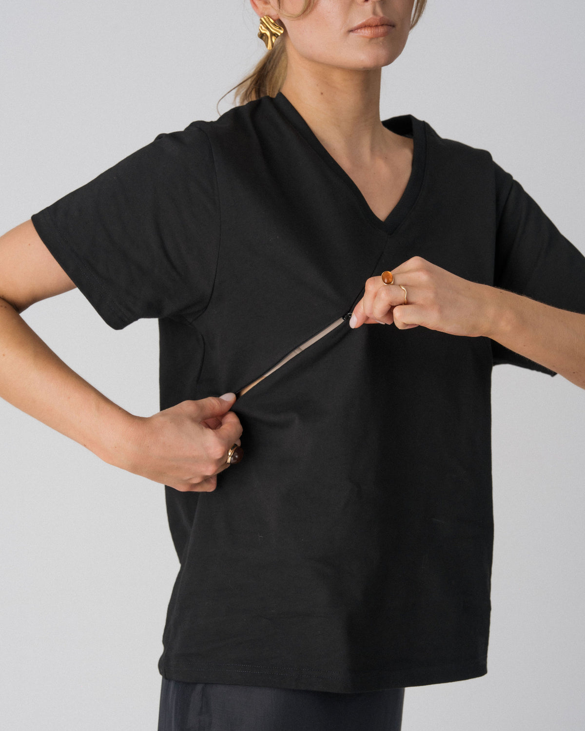Model opening the hidden diagonal zip below the V-neckline of the Lenelly Avery tee in black for discreet breastfeeding access