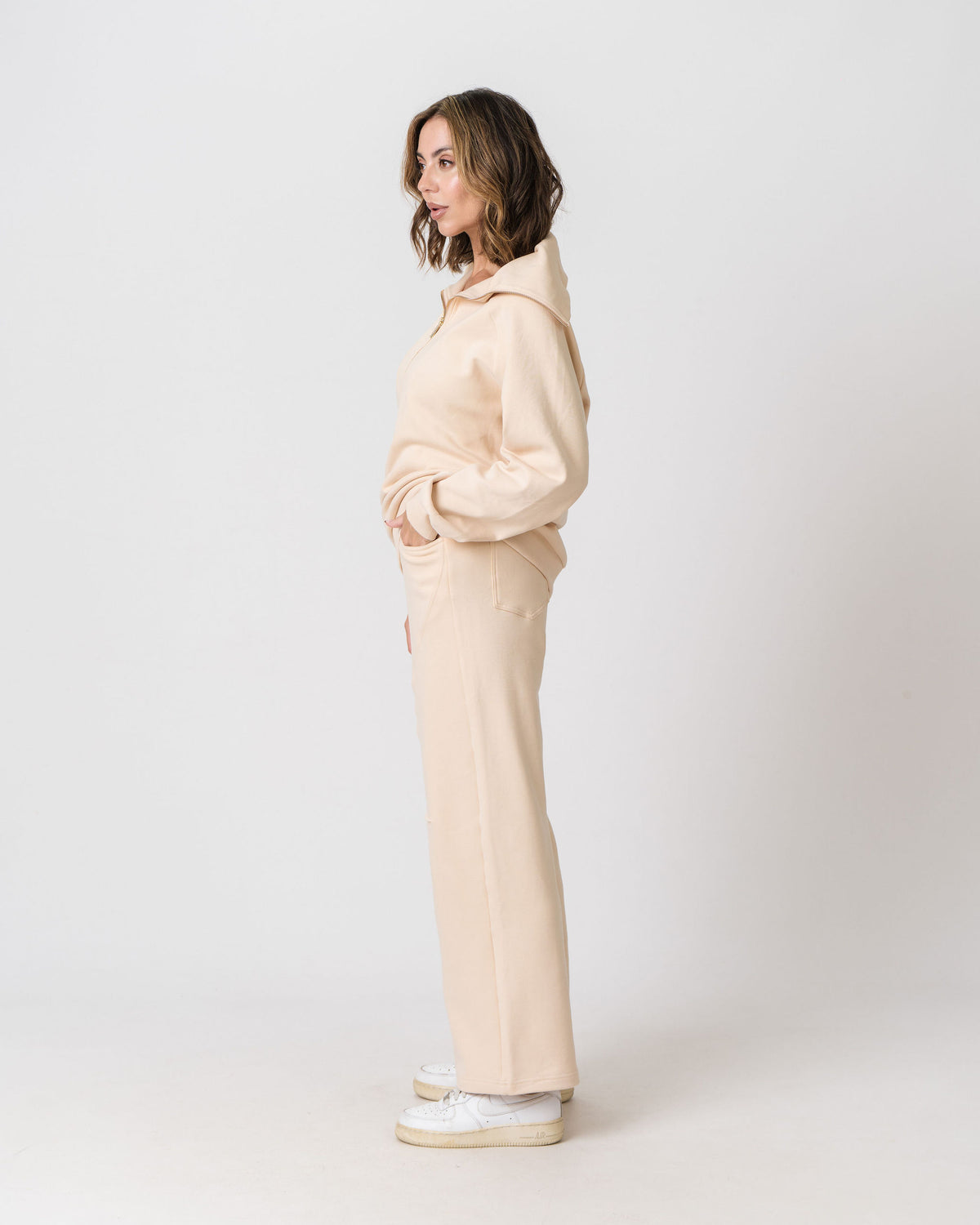 Lenelly Mish sweatpants in apricot worn with the matching Mish half zip sweatshirt, side view on a light studio background