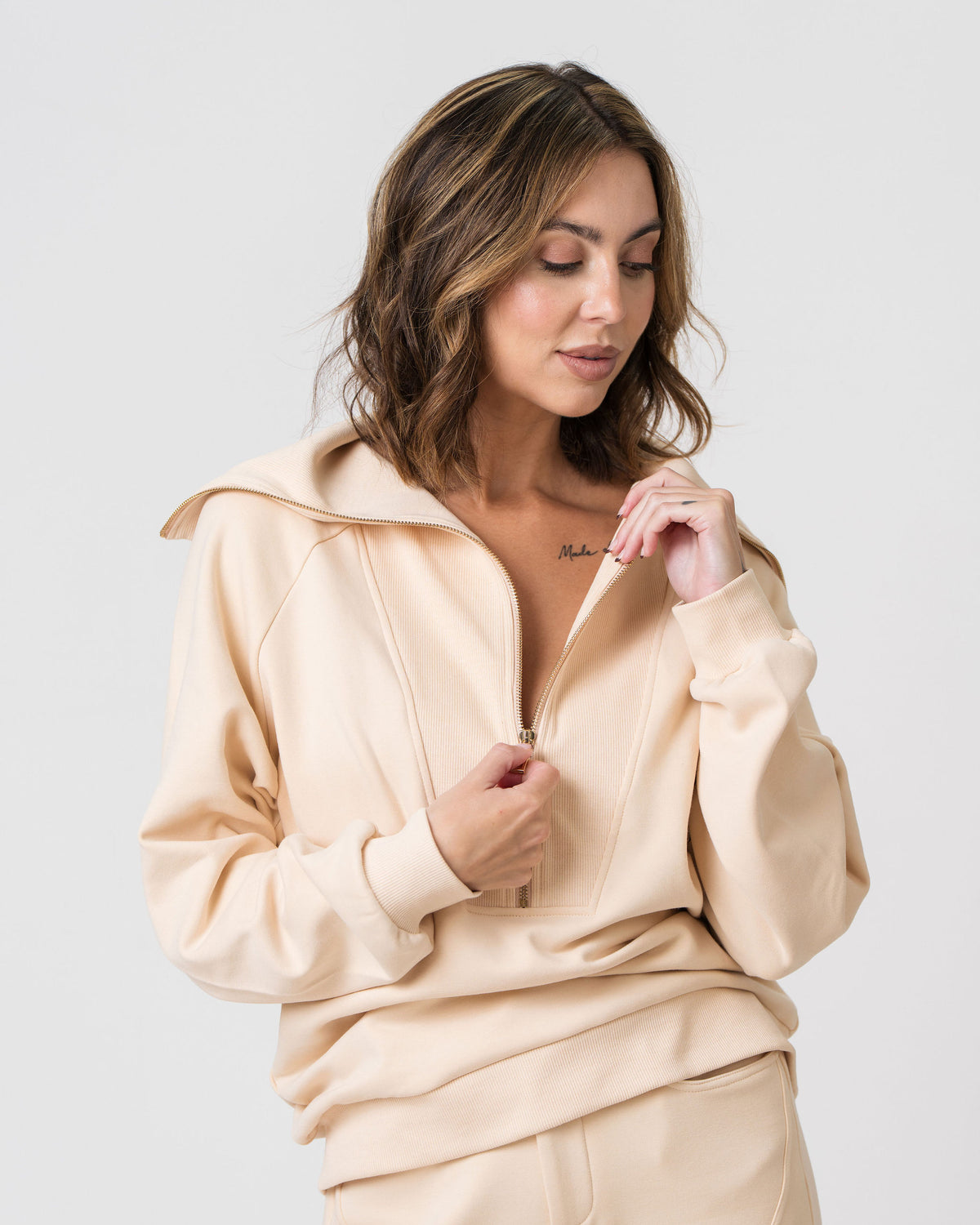Model unzipping the front zip on the Lenelly Mish half zip sweatshirt in apricot, showing the low zip for discreet breastfeeding access