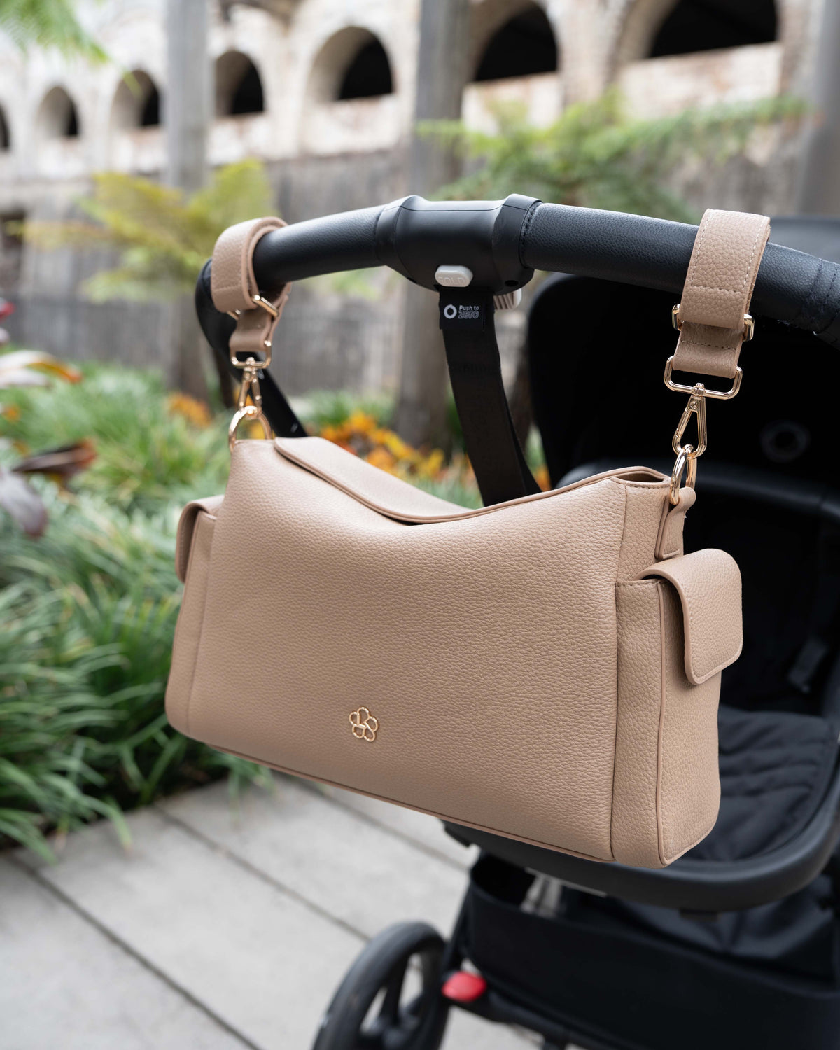 Lenelly Hera pram caddy bag in sand vegan leather with adjustable strap, hanging on a black stroller outdoors
