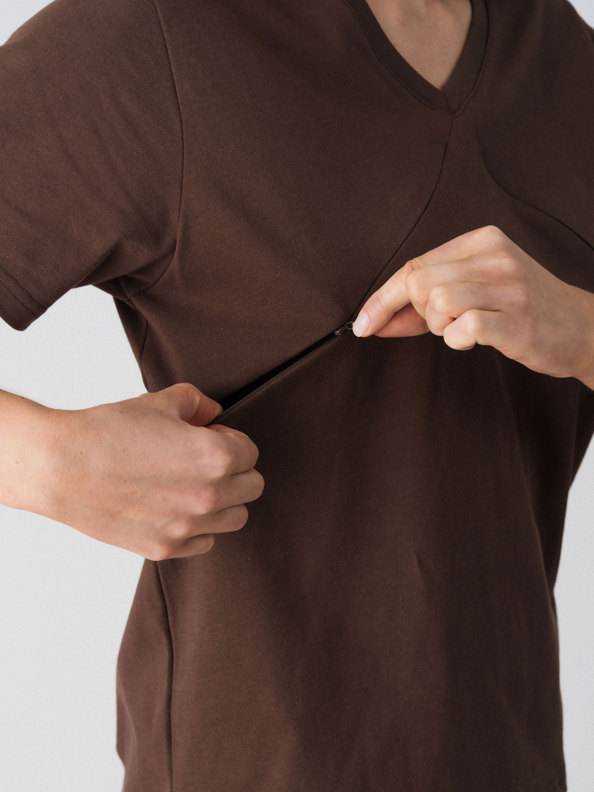 Model opening the hidden diagonal zip below the V-neckline of the Lenelly Avery tee in brown for discreet breastfeeding access
