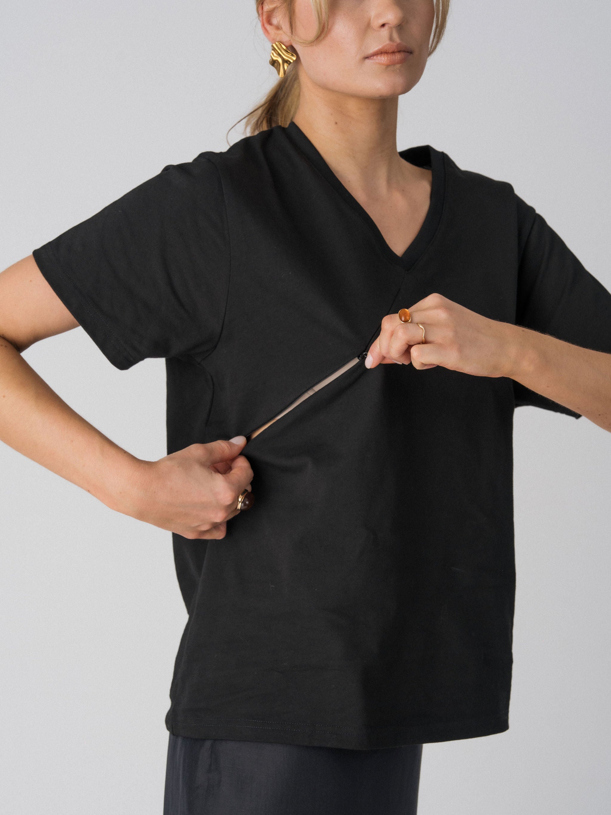 Model opening the hidden diagonal zip below the V-neckline of the Lenelly Avery tee in black for discreet breastfeeding access