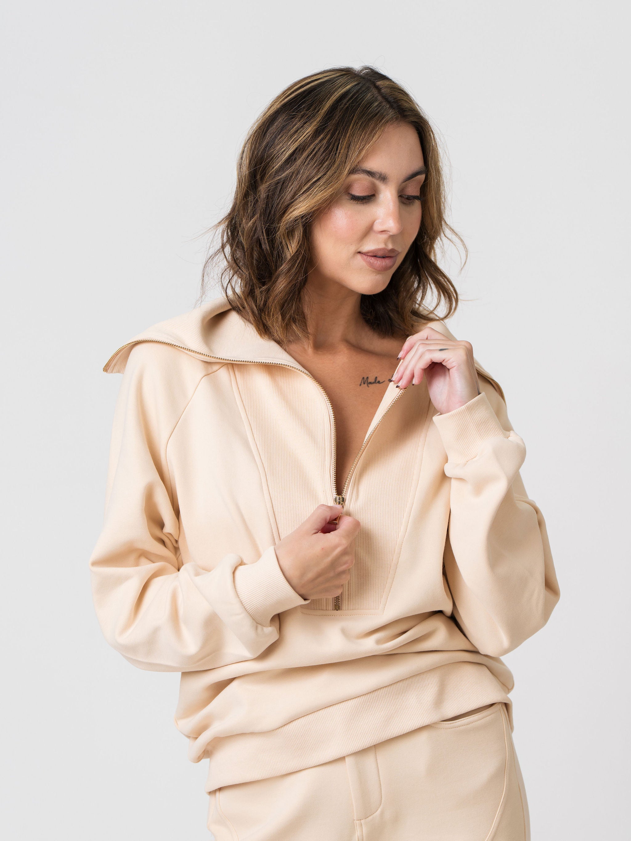 Model unzipping the front zip on the Lenelly Mish half zip sweatshirt in apricot, showing the low zip for discreet breastfeeding access