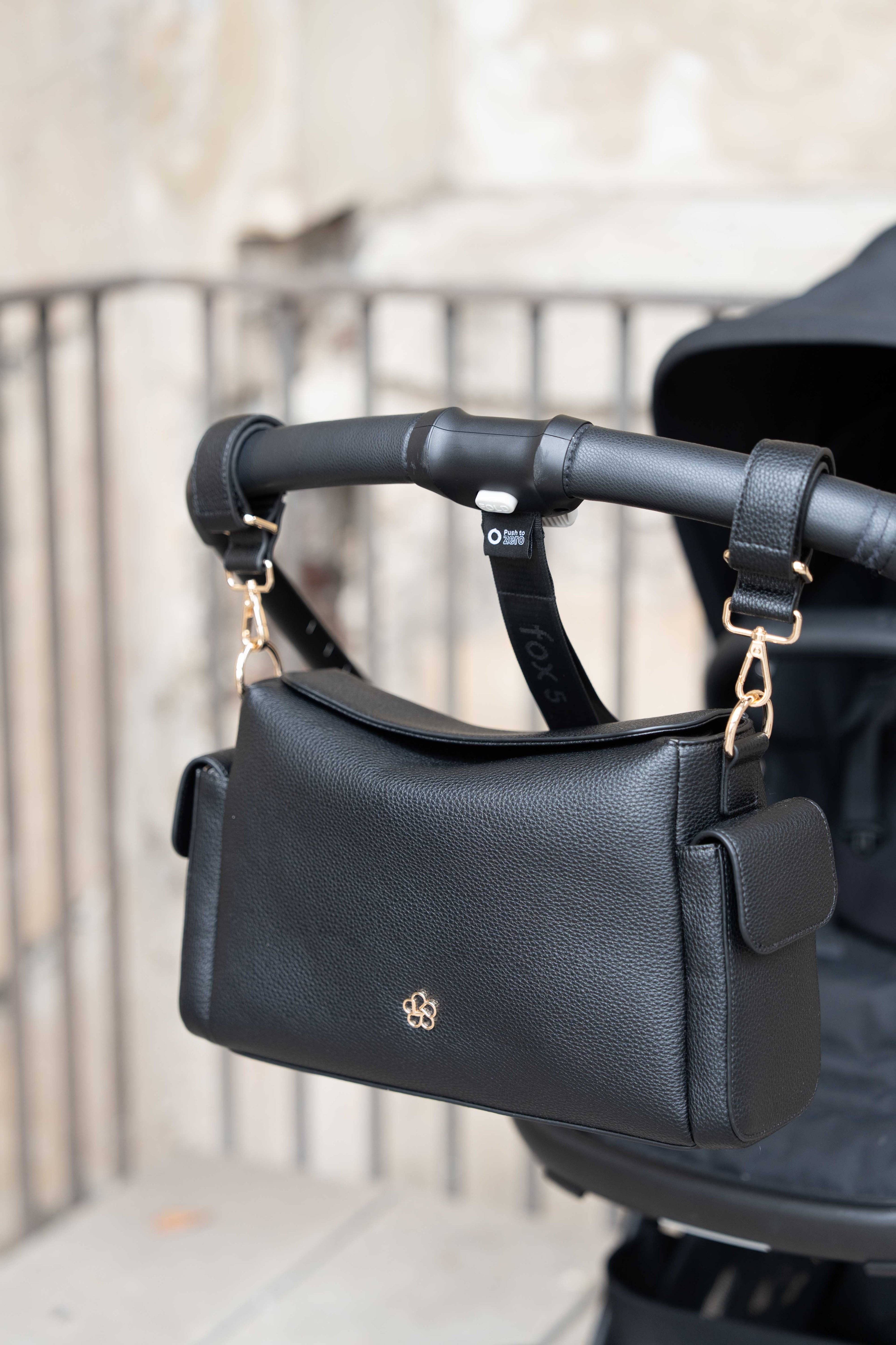 Lenelly Hera pram caddy bag in black vegan leather with adjustable strap, front view attached to a stroller with a blurred background