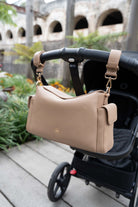 Lenelly Hera pram caddy bag in sand vegan leather with adjustable strap, hanging on a black stroller outdoors
